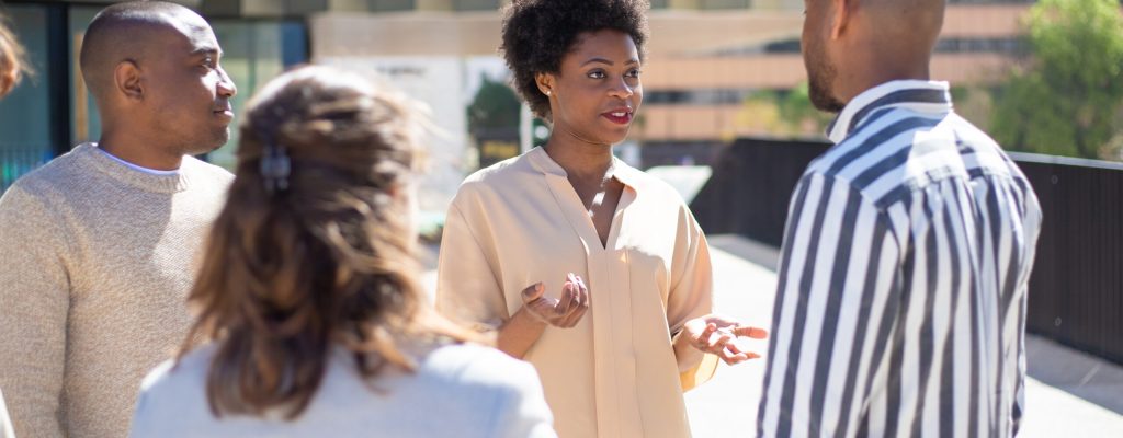Group of young friends standing on street and communicating. Smiling African American woman talking to friends. Communication concept
